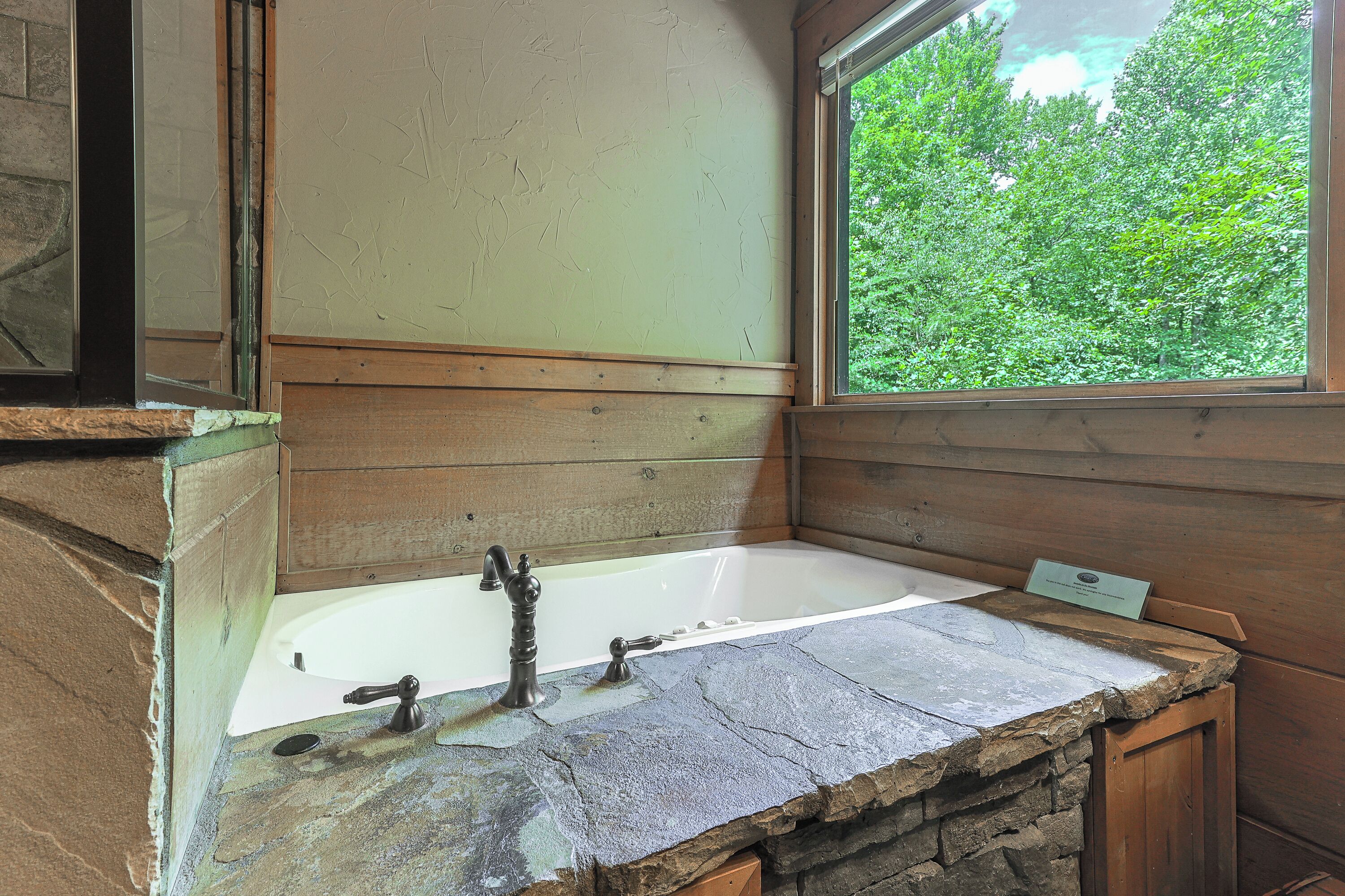A bathroom with a stone sink, a bathtub, and a window with a view of greenery.
