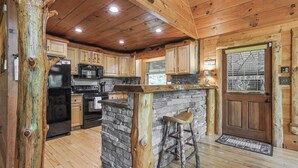A wooden cabin interior with a kitchen, stone island, and wooden bar stools. - Serenity on The Mountain | Blue Ridge, GA (Blue Ridge)