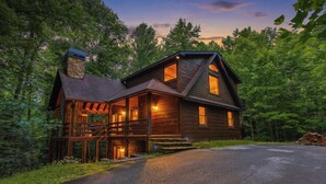 A wooden cabin with a porch, a chimney, and a driveway leading to the entrance. - Serenity on The Mountain | Blue Ridge, GA (Blue Ridge)