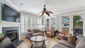 A living room with a fireplace, a ceiling fan, and a view of the outside. - Award-Winning Resort Amenities | Boardwalk at Grand Pavilion 113 (Isle of Palms)