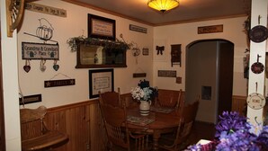 Un comedor con una mesa de madera, sillas y un jarrón de flores. Hay adornos en la pared, incluyendo letreros y cuadros enmarcados.