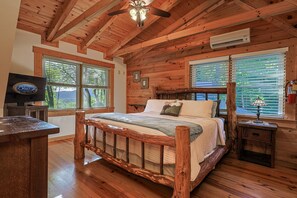 Quarto no estilo cabana com cama de madeira, ventilador de teto e janelas amplas.