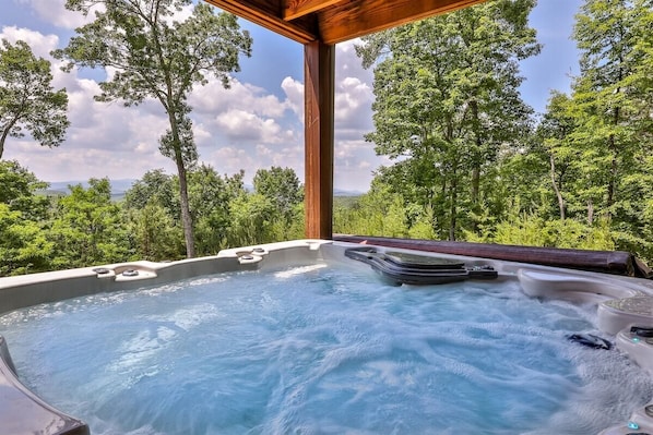 A hot tub with a wooden pergola, surrounded by lush greenery and trees.