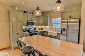 A kitchen with green cabinets, a stainless steel refrigerator, a wooden island, and pendant lighting. - Magnolia In The Mountains | Ellijay, GA (Ellijay)