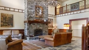 Lareira de pedra com mantelpiece, sofá e mesa de centro numa sala de estar ampla com teto alto e decoração na parede.