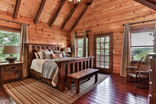 A wooden cabin interior with a bed, a bench, a table, and a chair.