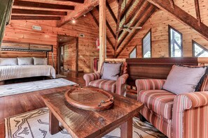 A log cabin interior with a bed, two striped sofas, a round wooden table, and a ceiling fan. - Fox Run Ridge | Ellijay, GA (Ellijay)
