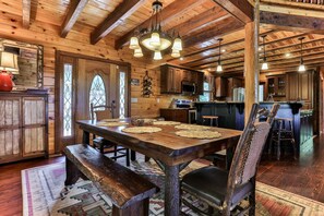 A rustic wooden interior with a dining table set for four, wooden beams on the ceiling, and a kitchen area in the background.