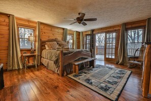 A log cabin bedroom with a bed, a ceiling fan, a rug, and a chair.