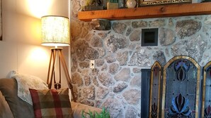 A cozy living room with a stone fireplace, a wooden ceiling, a patterned rug, and a sofa with cushions. -  Cozy Lake Front Cottage w/dock, perfect family retreat! (Camdenton)