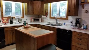 A kitchen with wooden cabinets, a central island, a sink, a toaster, and a coffee maker. -  Cozy Lake Front Cottage w/dock, perfect family retreat! (Camdenton)