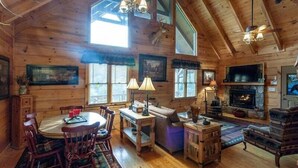 A log cabin interior with a dining area, seating, a fireplace, and a television. - Water's Edge | Blue Ridge, GA (Blue Ridge)