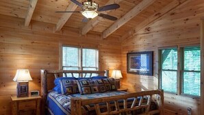 A wooden cabin bedroom with a bed, two nightstands, a ceiling fan, and windows. - Water's Edge | Blue Ridge, GA (Blue Ridge)