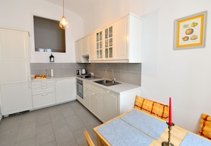 A modern kitchen with white cabinetry, a built-in oven, a sink, and a dining area with a table and chairs.