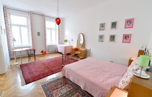 A bedroom with a bed, a desk, a chair, a rocking horse, a mirror, and several framed pictures on the wall.