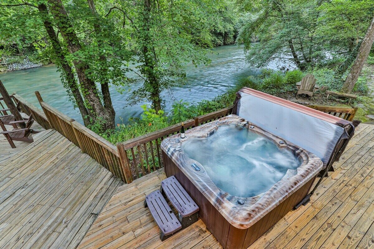 Een houten terras met een jacuzzi, houten stoelen en uitzicht op een rivier.