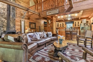 A log cabin interior with a stone wall, a fireplace, a wooden dining area, and a cozy seating area.