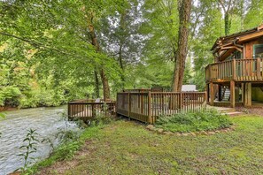 A cabin with a deck overlooking a river, surrounded by dense forest.