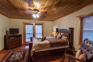 A bedroom with a wooden ceiling, a bed with a headboard, a television on a wooden dresser, and a window with blinds. - Paradise Too | Ellijay, GA (Ellijay)