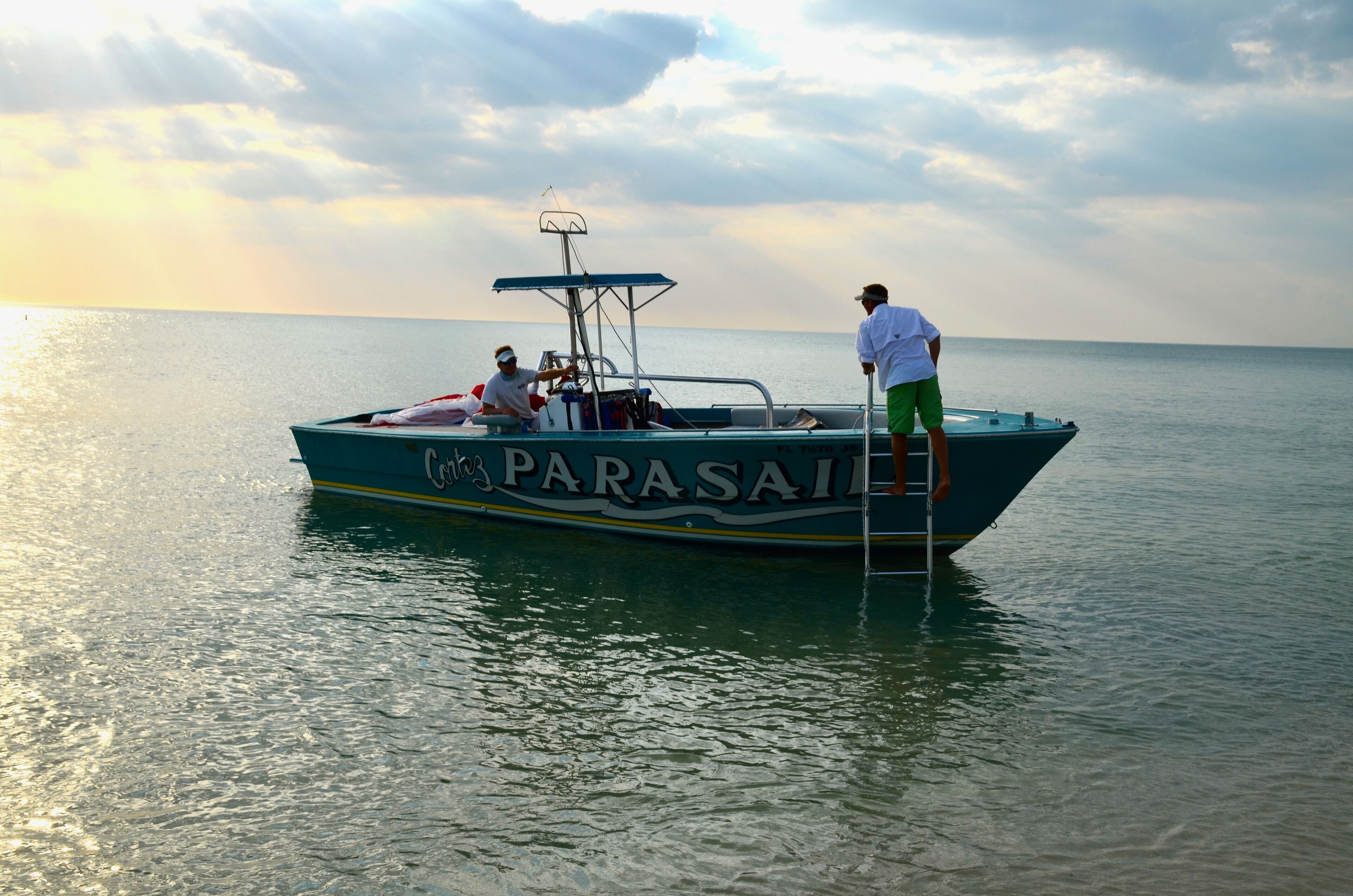 A boat named 'Parasail' with two people on board, one standing and one seated, on calm water.