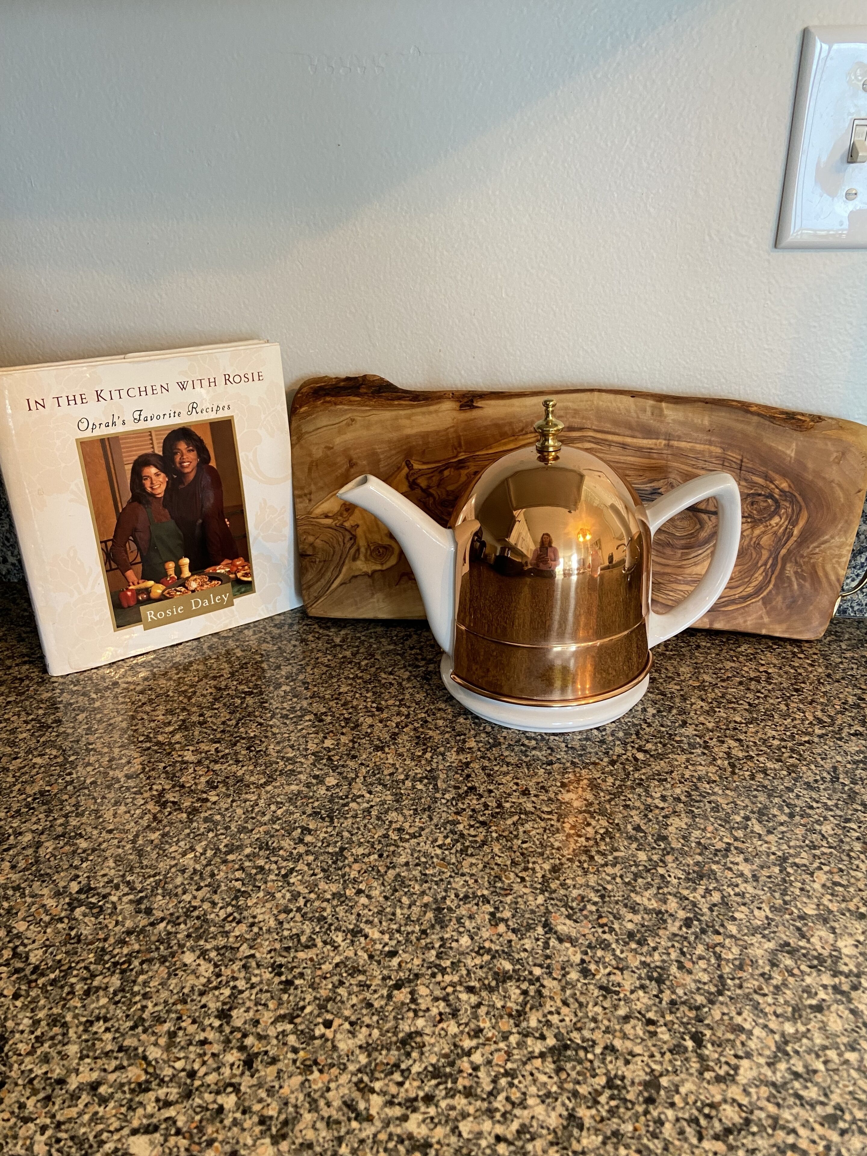 A kitchen counter with a teapot and a cookbook titled "In the Kitchen with Rosie".