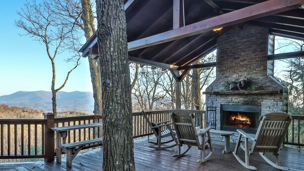 Eine Holzterrasse mit Kamin aus Stein, Schaukelstühlen und einer Bank.