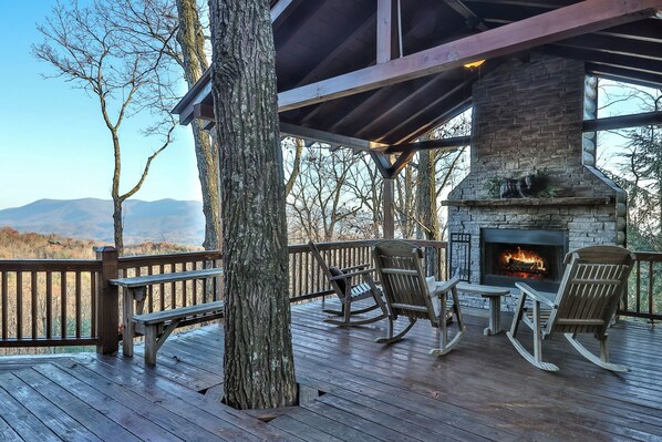 A wooden deck with a stone fireplace, rocking chairs, and a bench.