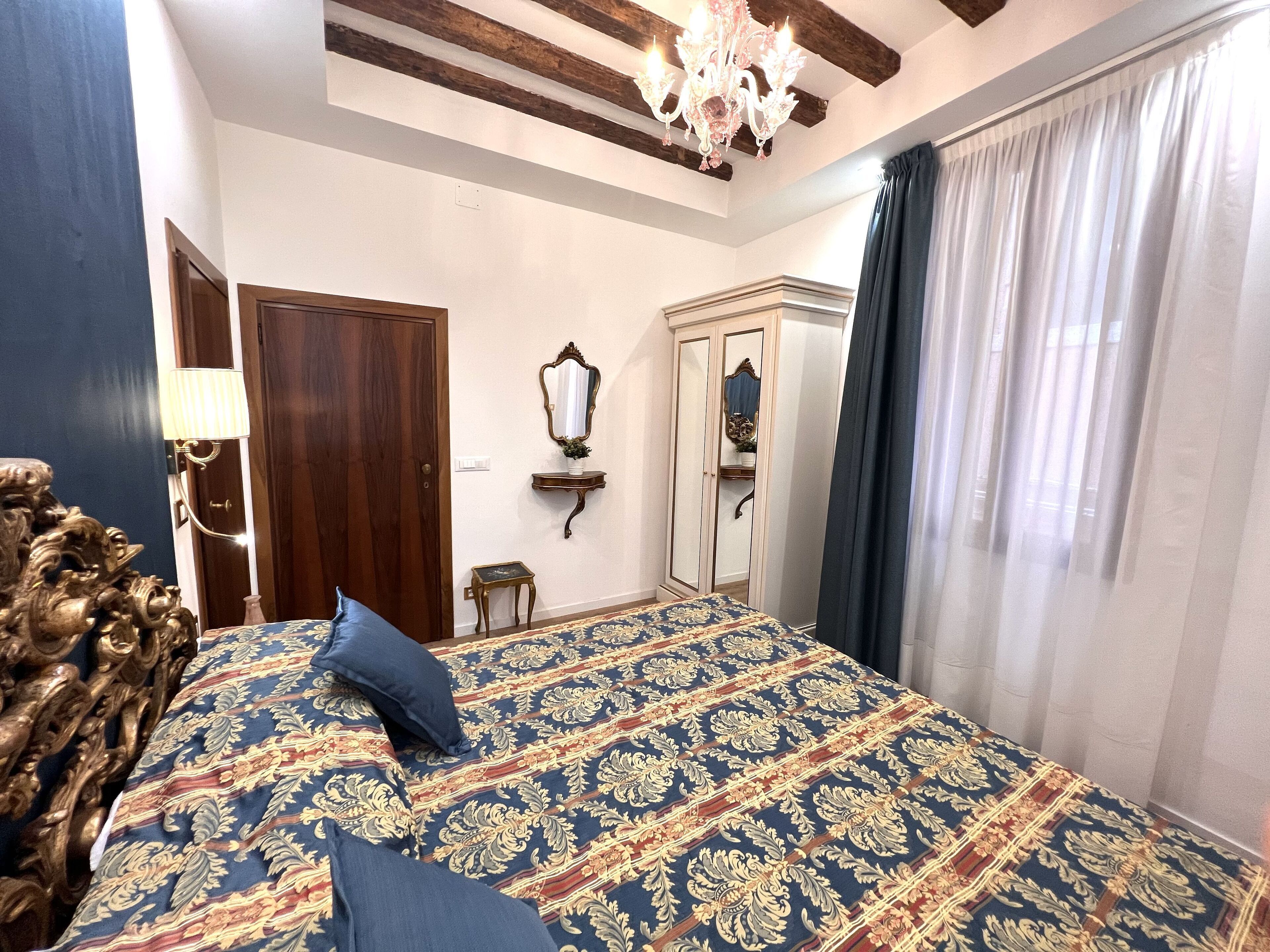 Une chambre à coucher avec un grand lit, une armoire en bois, un miroir et un lustre.