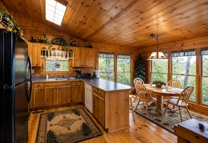 A cabin-style kitchen with wooden cabinets, a refrigerator, a coffee maker, and a dining area with a table and chairs.