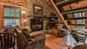 L’intérieur d’une cabane en rondins, avec une cheminée en pierre, des meubles en bois et un escalier.