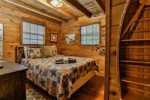 A wooden cabin room with a bed, a desk, and a staircase. - Creekside Reflections | Blue Ridge, GA (Blue Ridge)