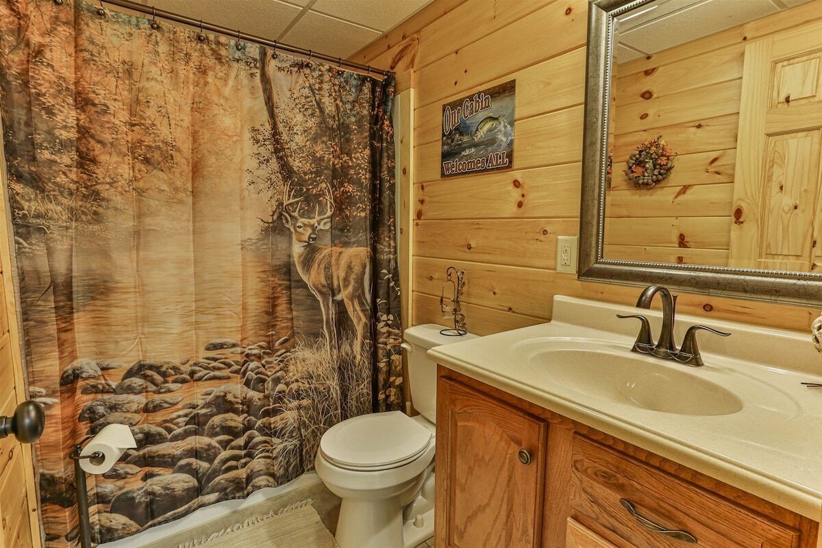 Baño con un mural de ciervo, un letrero de cabaña de madera, un lavabo y un espejo.