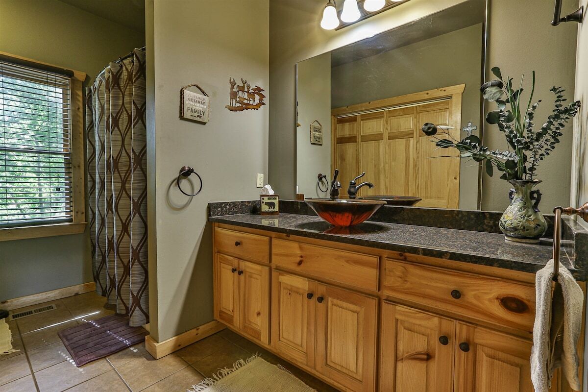 A bathroom with wooden cabinets, a large mirror, a sink with a decorative bowl, and a shower with a patterned curtain.