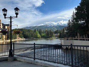 A riverside view with a bridge, mountains, and a lamppost with flower baskets. - Ski-in/out One-Bd. Condo, Village at Breckenridge, Steps to Main St., Sleeps 2-6 (Breckenridge)