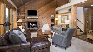 Ein gemütliches Wohnzimmer mit Kamin, Ledersofa und Ohrensessel mit Hunde-Zahn-Muster.