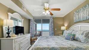 A bedroom with a large bed, a ceiling fan, a TV, and a view of the ocean through a balcony. - Sea Watch VIII 102 - Two Bedroom, Two Bath Oceanfront Condo (Garden City Beach)