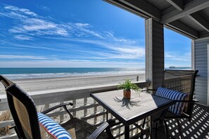A balcony with a view of the beach and ocean, a table with a plant, and two chairs with striped cushions. - Sea Watch VIII 102 - Two Bedroom, Two Bath Oceanfront Condo (Garden City Beach)