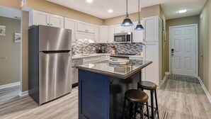 A modern kitchen with white cabinets, stainless steel appliances, a central island with stools, and pendant lighting. - Sea Watch VIII 102 - Two Bedroom, Two Bath Oceanfront Condo (Garden City Beach)