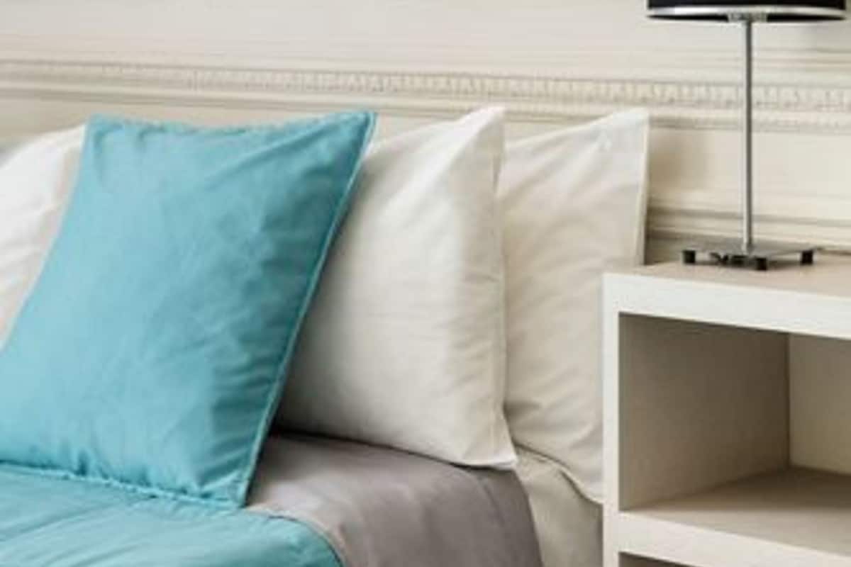 A neatly arranged bedroom with a bed, pillows, a bedside table, and a lamp.