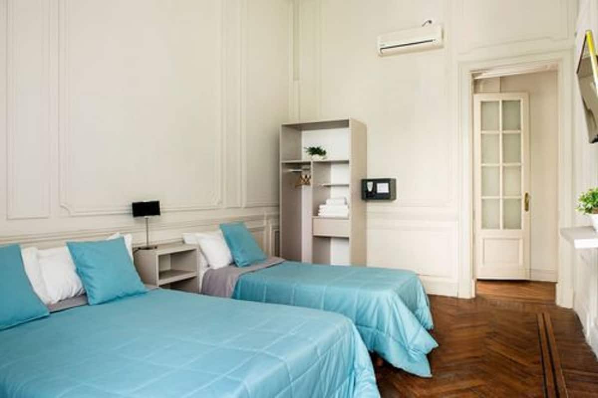 A bedroom with two beds, a wardrobe, a bedside table, and a mirror.