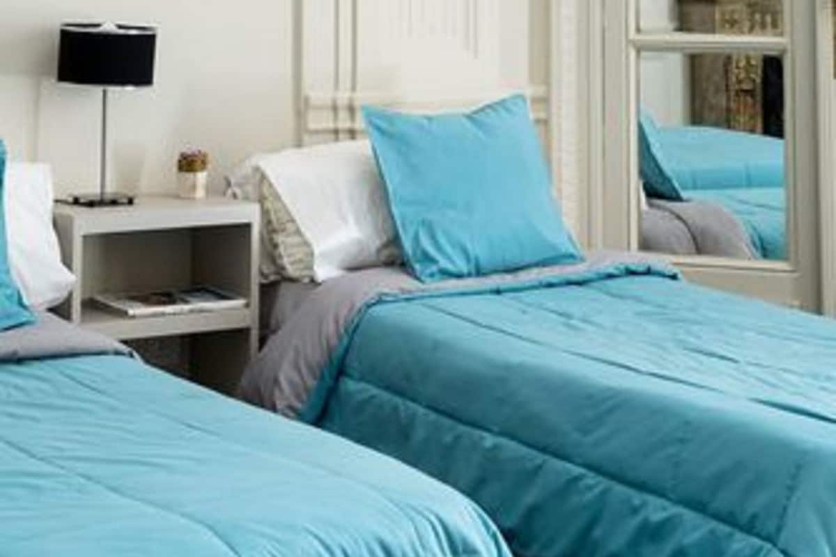 A bedroom with two beds, a bedside table, a lamp, and a mirror.