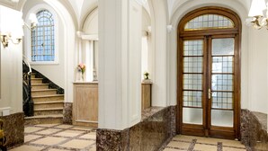A grand hallway with marble flooring, a staircase, and a large wooden door with glass panels. - Patios de Recoleta (Buenos Aires)
