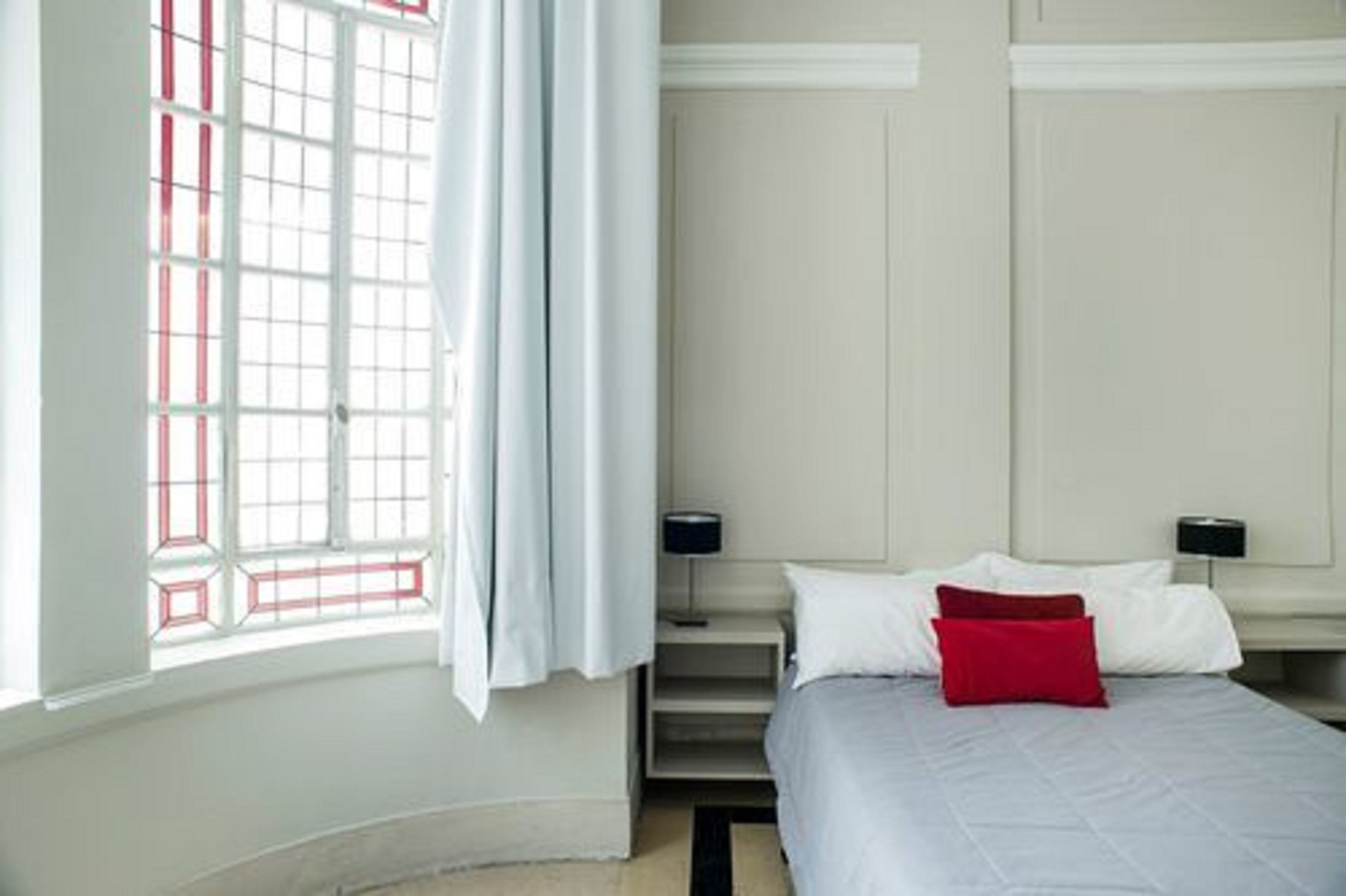 A bedroom with a bed, a nightstand, a lamp, and a window with curtains.