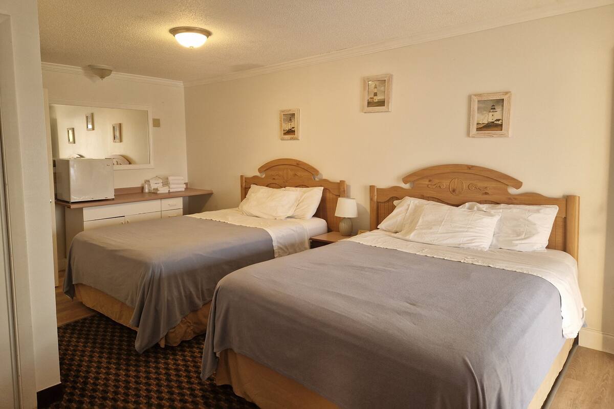 A hotel room with two single beds, a small desk with a mirror, and a patterned rug.