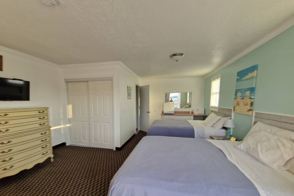 A hotel room with two beds, a dresser, a television, and a bathroom visible through an open door.