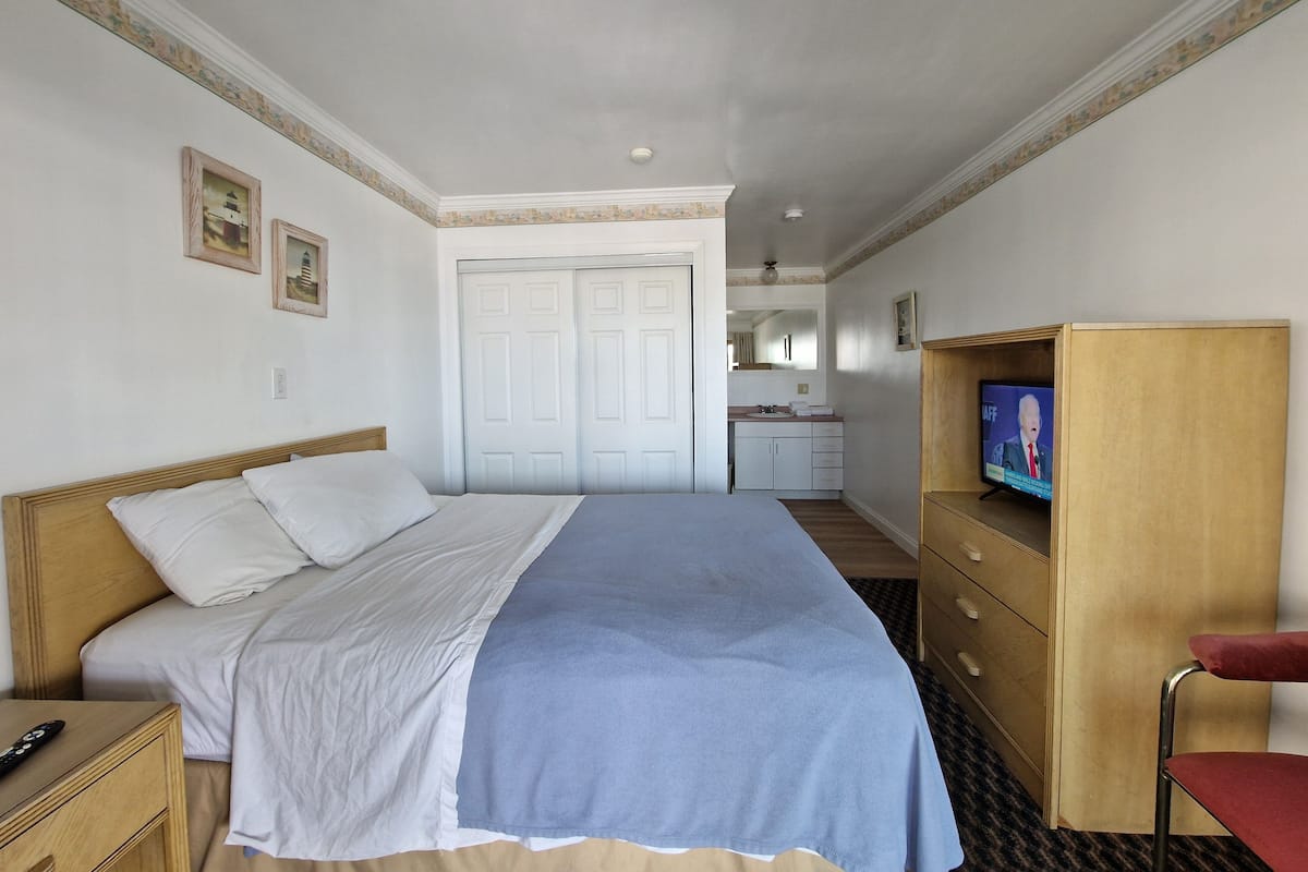 A hotel room with a bed, a wooden nightstand, a television, a desk, and a chair.