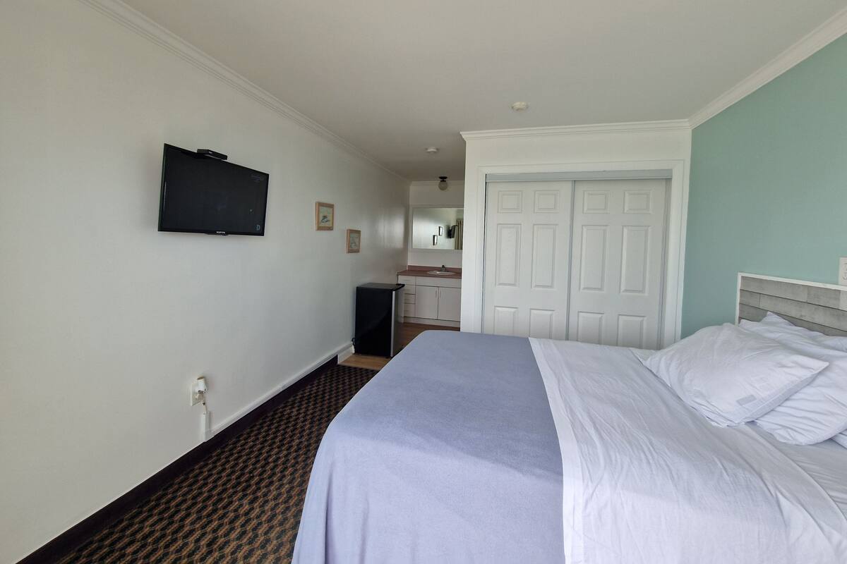A hotel room with a bed, a television mounted on the wall, a bathroom with a sink and mirror, and a closet with a door.
