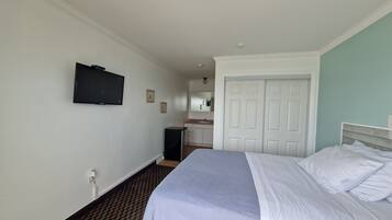 A hotel room with a bed, a television mounted on the wall, a bathroom with a sink and mirror, and a closet with a door.