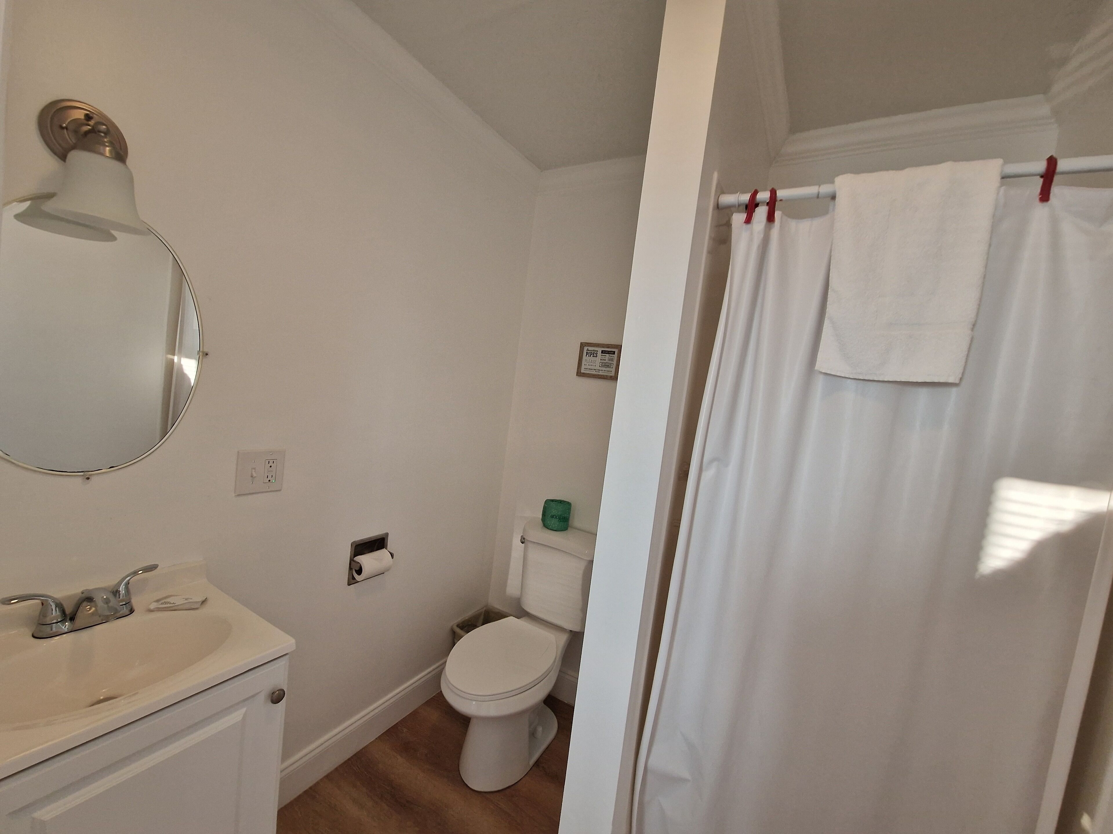 A bathroom with a white sink, mirror, toilet, and shower curtain.