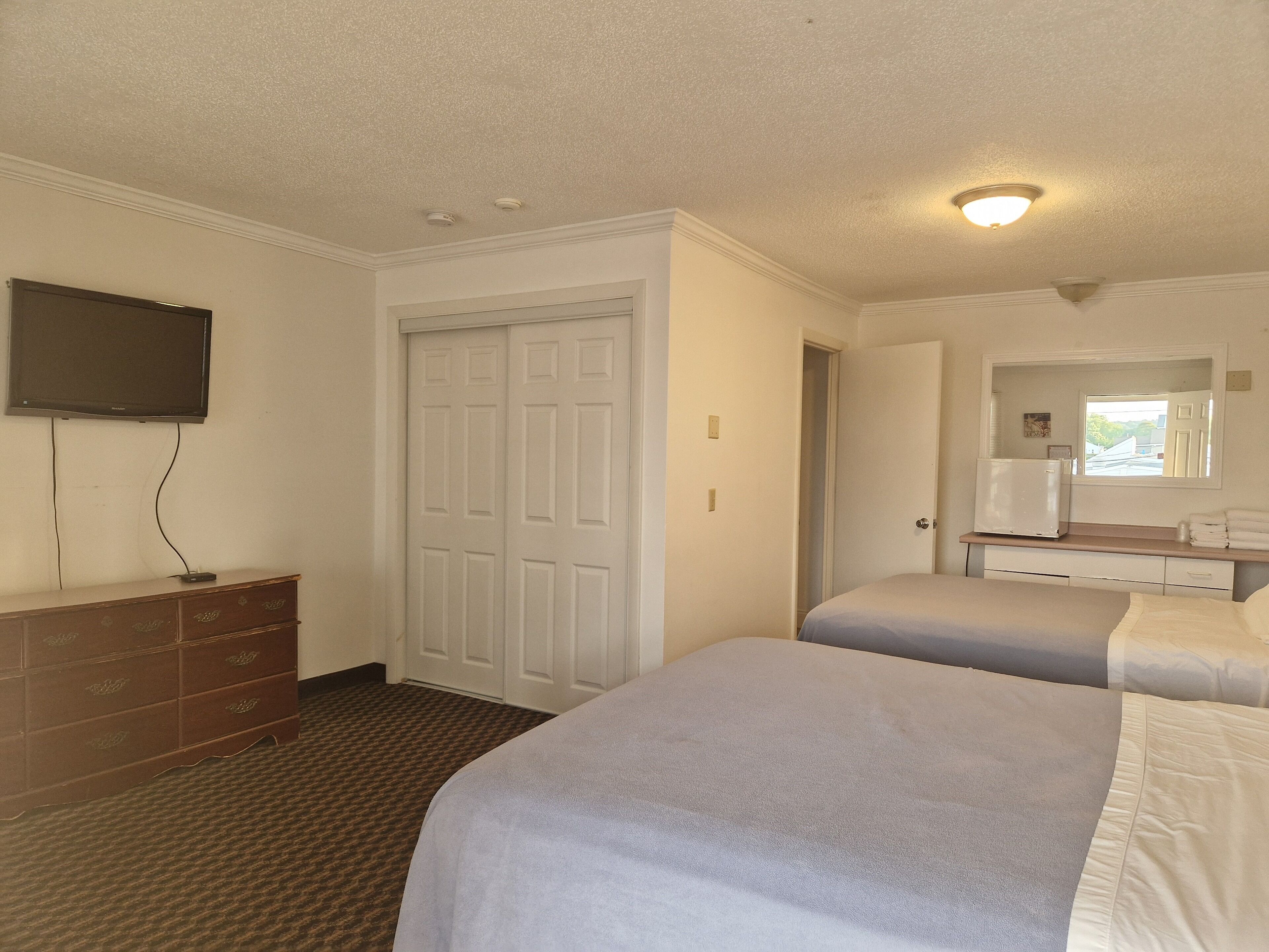 Habitación de hotel con dos camas, una cómoda, un televisor montado en la pared y una puerta que da a otra habitación.